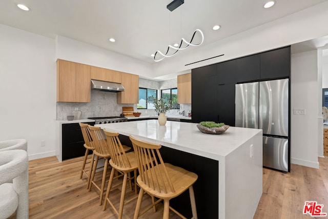 kitchen featuring hanging light fixtures, a kitchen island, stainless steel refrigerator, light hardwood / wood-style floors, and extractor fan