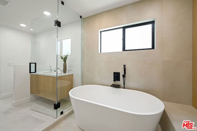 bathroom featuring vanity, independent shower and bath, and tile walls