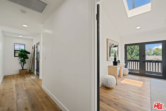 entryway featuring vaulted ceiling with skylight, french doors, and light wood-type flooring