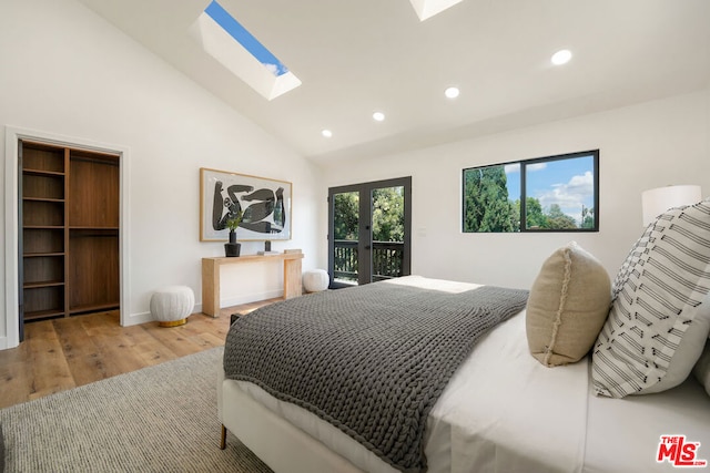 bedroom with access to exterior, a walk in closet, light wood-type flooring, a skylight, and high vaulted ceiling