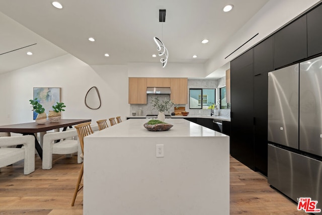 kitchen featuring appliances with stainless steel finishes, decorative light fixtures, a kitchen island, and light hardwood / wood-style floors