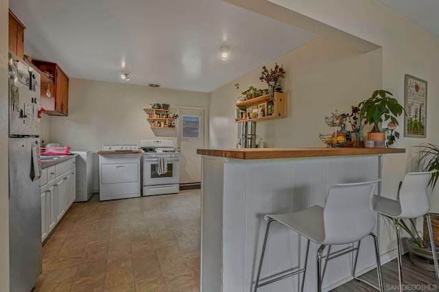 kitchen featuring washer / dryer, stainless steel fridge, white cabinetry, white gas stove, and a kitchen bar