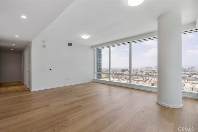 unfurnished room featuring decorative columns and light wood-type flooring