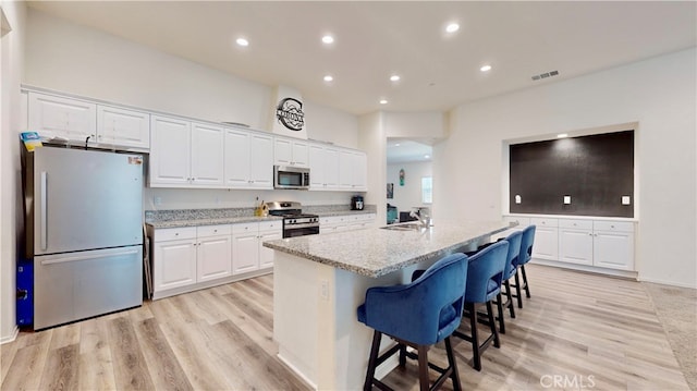 kitchen with white cabinetry, light hardwood / wood-style floors, stainless steel appliances, and an island with sink