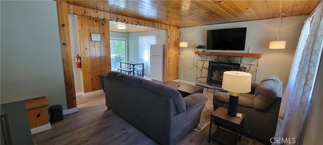 living room with a stone fireplace, wood ceiling, hardwood / wood-style floors, and wood walls