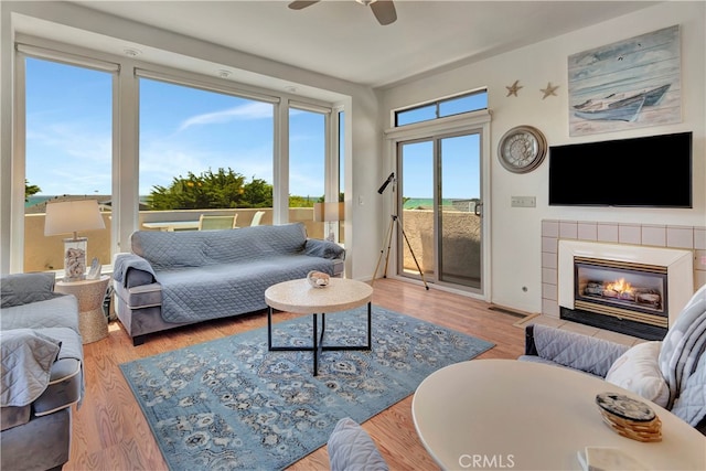 living room featuring a tiled fireplace, wood-type flooring, and ceiling fan