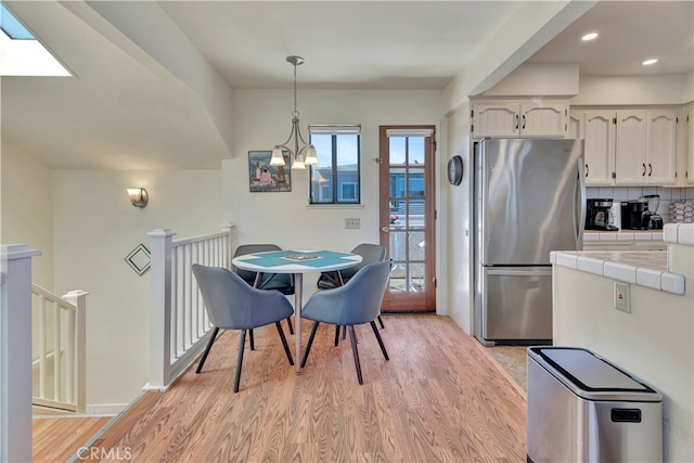 kitchen featuring stainless steel fridge, light hardwood / wood-style floors, decorative light fixtures, tile counters, and decorative backsplash