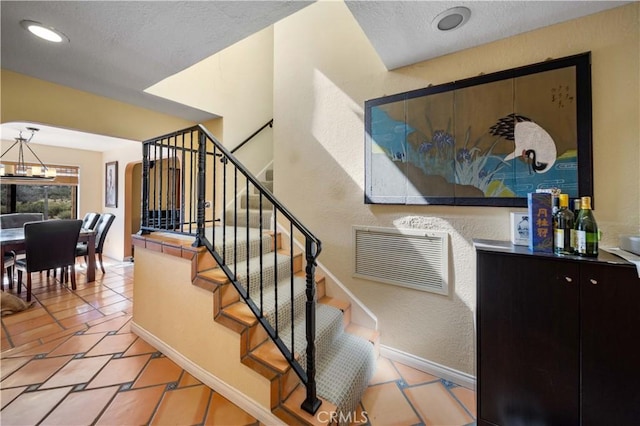 stairway with tile patterned floors, a textured ceiling, and a notable chandelier