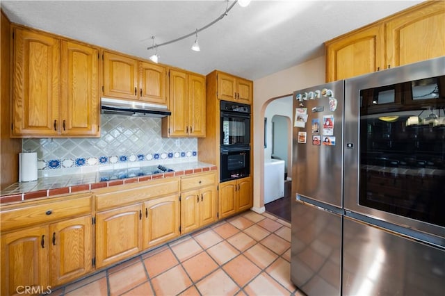 kitchen featuring tile countertops, light tile patterned floors, tasteful backsplash, cooktop, and stainless steel refrigerator