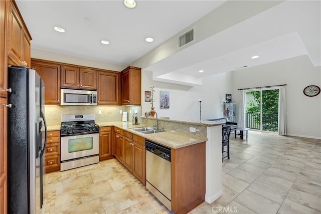 kitchen featuring kitchen peninsula, appliances with stainless steel finishes, decorative backsplash, light stone countertops, and sink