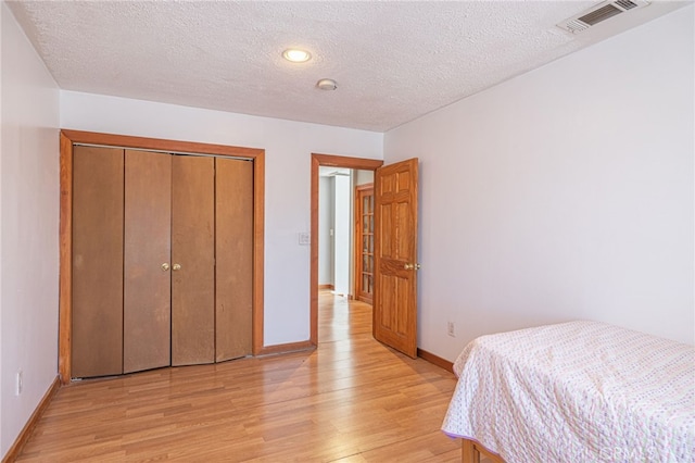 bedroom with a closet, a textured ceiling, and light wood-type flooring