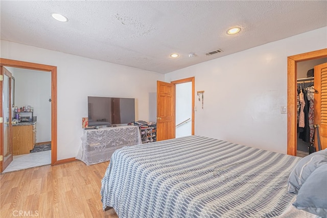 bedroom featuring a spacious closet, a textured ceiling, light wood-type flooring, and a closet