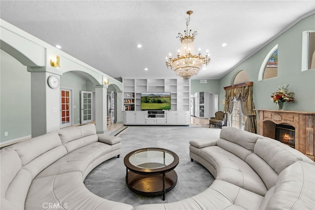 living room featuring a textured ceiling, built in shelves, light carpet, a stone fireplace, and a chandelier