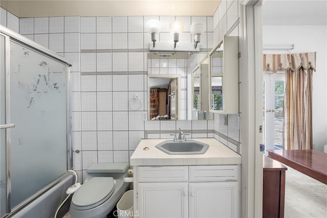 full bathroom with backsplash, toilet, vanity, and shower / bath combination with glass door