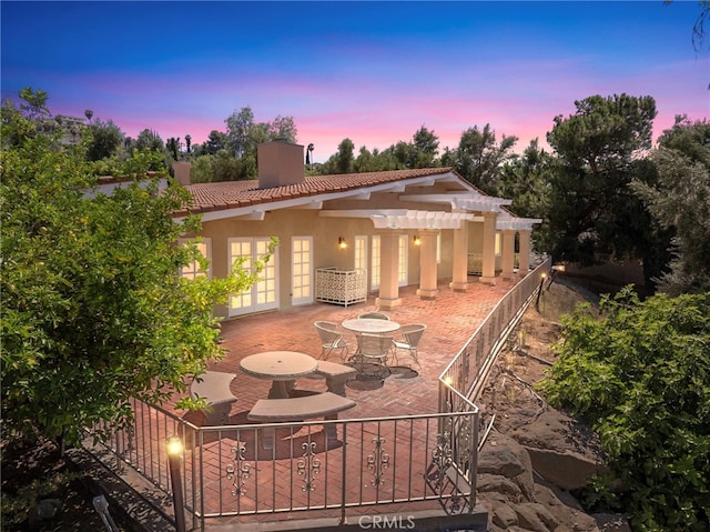 back house at dusk with french doors, a pergola, and a patio