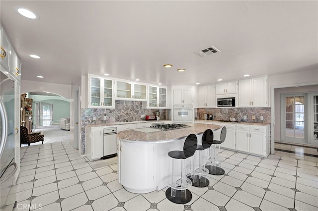 kitchen with appliances with stainless steel finishes, a kitchen island, white cabinetry, tasteful backsplash, and a kitchen breakfast bar