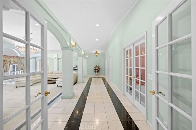 corridor with a textured ceiling, ornate columns, french doors, light tile patterned flooring, and crown molding