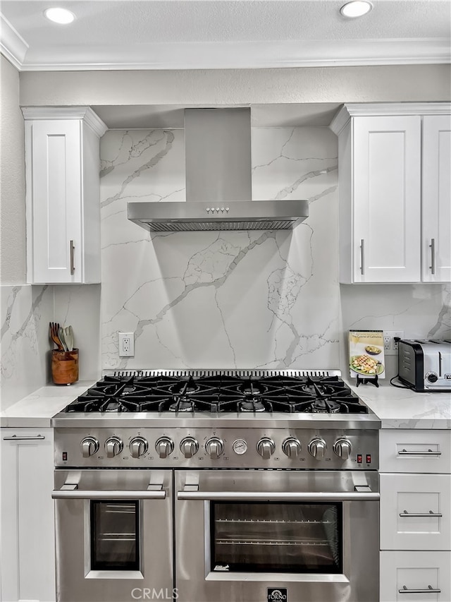 kitchen with decorative backsplash, white cabinets, wall chimney range hood, and range with two ovens