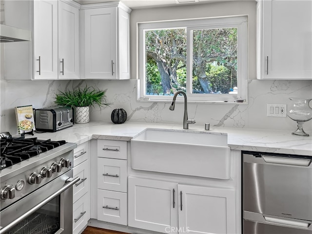 kitchen with white cabinets, light stone counters, sink, range hood, and stainless steel appliances