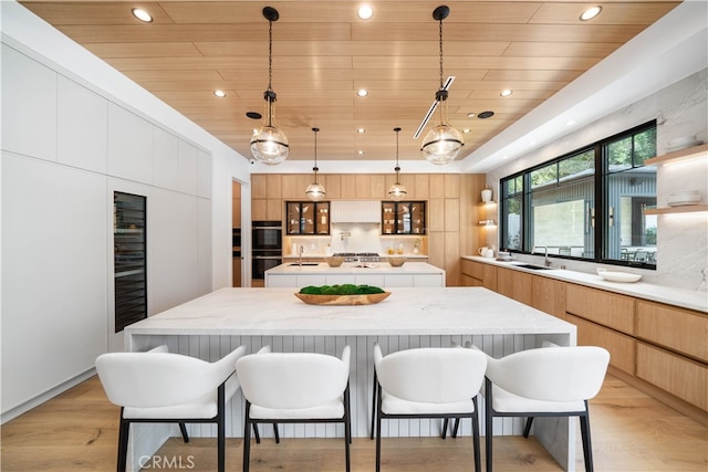 kitchen with decorative light fixtures, light brown cabinetry, light hardwood / wood-style floors, a kitchen island, and sink