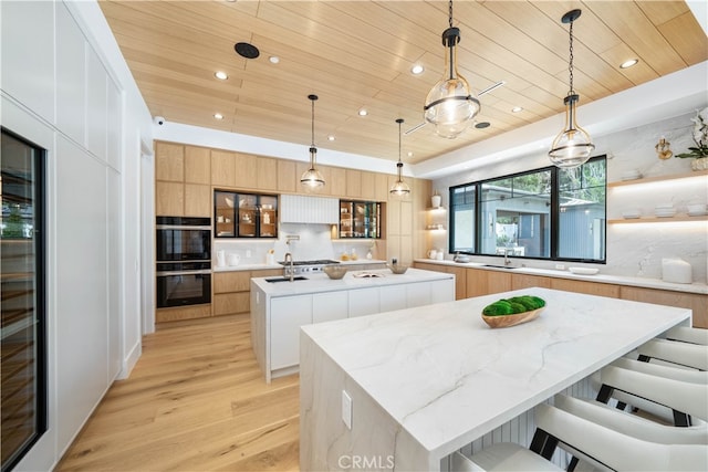 kitchen with black double oven, light brown cabinetry, light hardwood / wood-style flooring, hanging light fixtures, and a large island