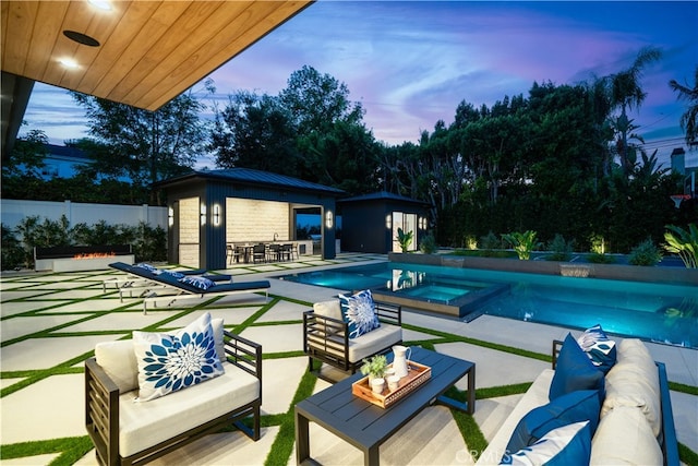 pool at dusk with outdoor lounge area, an in ground hot tub, and a patio area