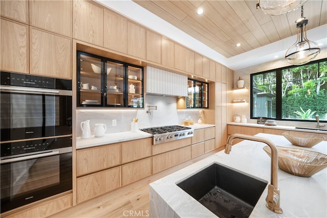 kitchen with hanging light fixtures, light wood-type flooring, stainless steel gas stovetop, black double oven, and light brown cabinetry