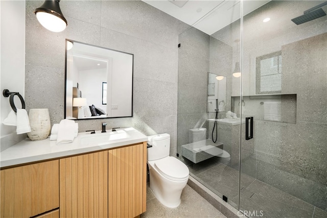 bathroom with vanity with extensive cabinet space, tile walls, toilet, and a shower with door