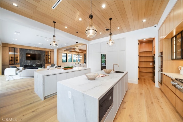 kitchen with a kitchen island with sink, light wood-type flooring, white cabinets, sink, and pendant lighting