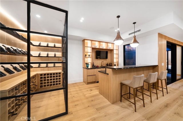 kitchen featuring kitchen peninsula, hanging light fixtures, a breakfast bar area, light wood-type flooring, and dark stone countertops