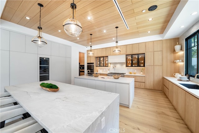 kitchen featuring a kitchen breakfast bar, a spacious island, light hardwood / wood-style flooring, pendant lighting, and light brown cabinetry