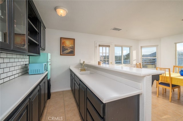 kitchen with decorative backsplash, kitchen peninsula, sink, and light tile patterned floors