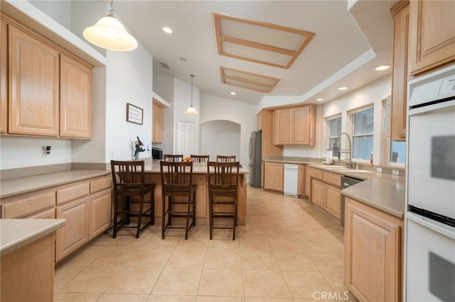 kitchen featuring sink, hanging light fixtures, a kitchen breakfast bar, white appliances, and light brown cabinetry