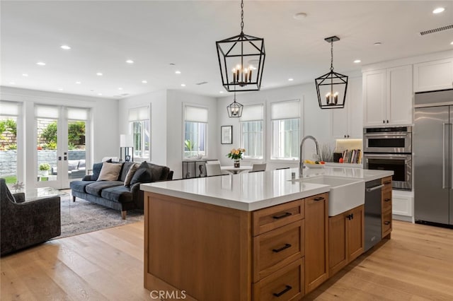 kitchen featuring an island with sink, appliances with stainless steel finishes, light wood-type flooring, pendant lighting, and sink