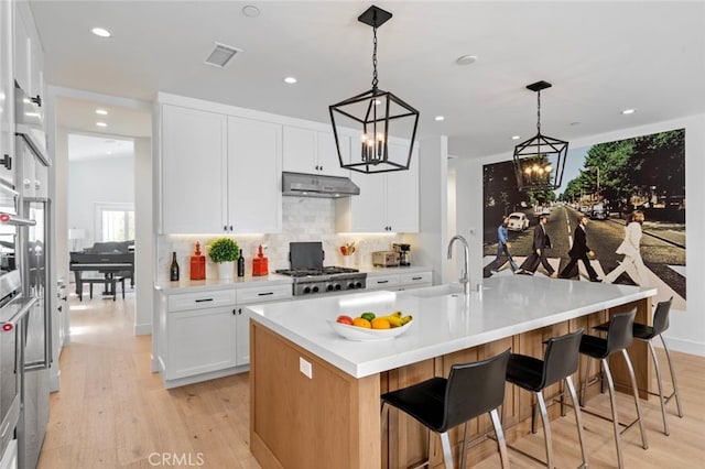 kitchen with white cabinets, a center island with sink, a breakfast bar area, light hardwood / wood-style flooring, and pendant lighting