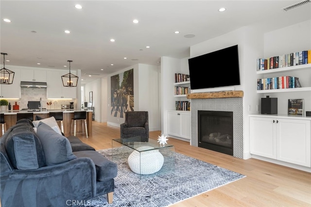 living room featuring a tiled fireplace, a notable chandelier, light wood-type flooring, and built in shelves