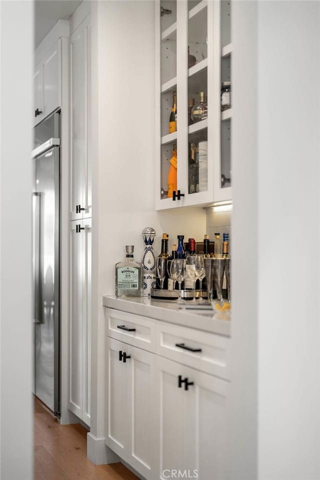 bar with white cabinetry, light wood-type flooring, and built in refrigerator