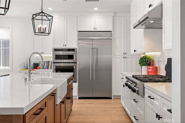 kitchen with light stone countertops, appliances with stainless steel finishes, decorative light fixtures, white cabinets, and light hardwood / wood-style flooring