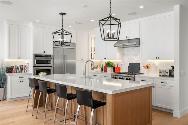 kitchen with white cabinetry, light hardwood / wood-style floors, an island with sink, and backsplash