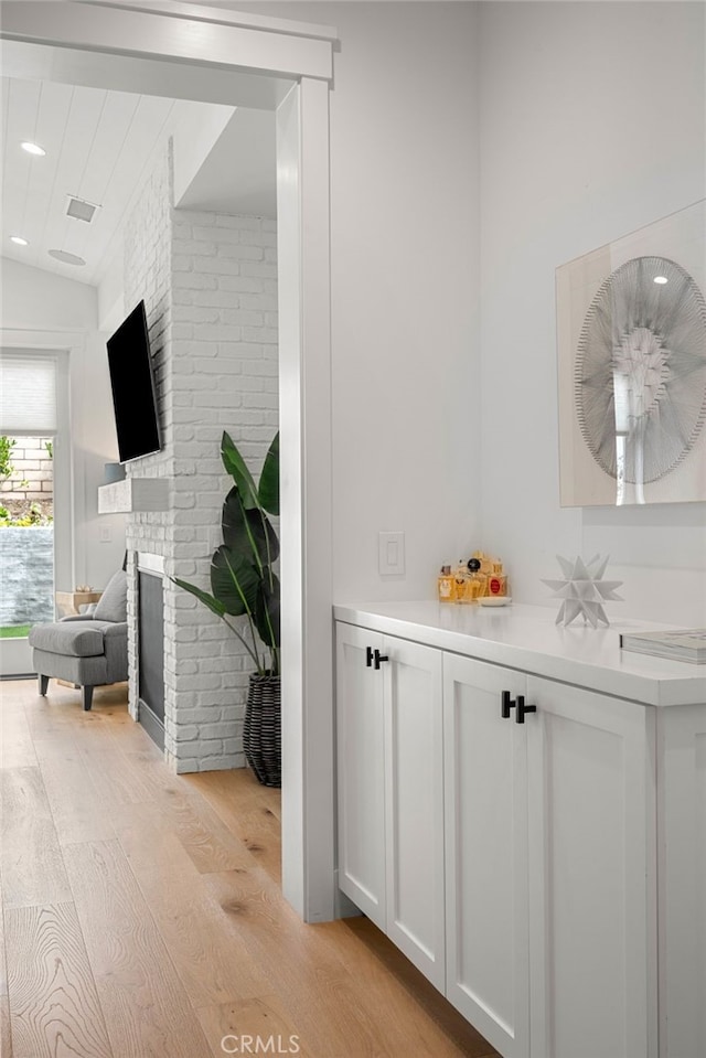 bathroom with hardwood / wood-style flooring, lofted ceiling, a brick fireplace, and brick wall