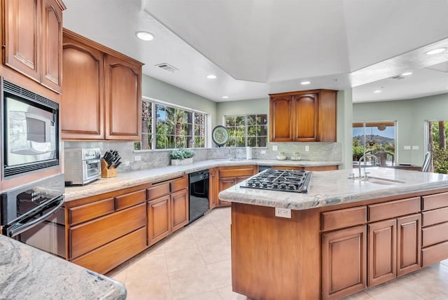 kitchen with visible vents, light stone countertops, tasteful backsplash, a sink, and black appliances