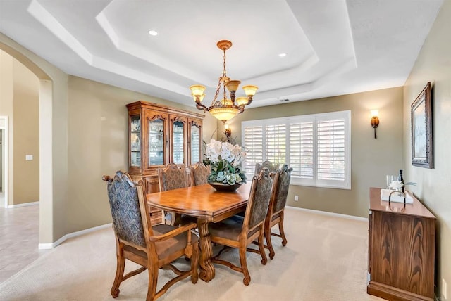 dining room featuring an inviting chandelier, light carpet, arched walkways, baseboards, and a tray ceiling