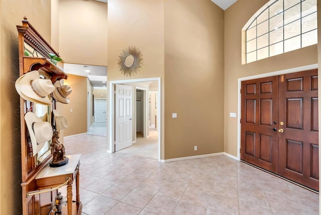 foyer with light tile patterned floors, baseboards, and a towering ceiling