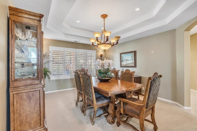 dining area featuring arched walkways, a tray ceiling, a notable chandelier, and light carpet