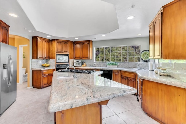 kitchen with light stone counters, an island with sink, recessed lighting, decorative backsplash, and black appliances