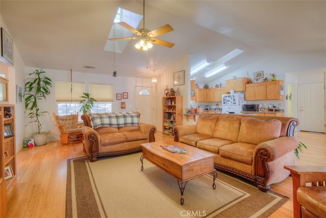 living room with lofted ceiling with skylight, light hardwood / wood-style floors, and ceiling fan