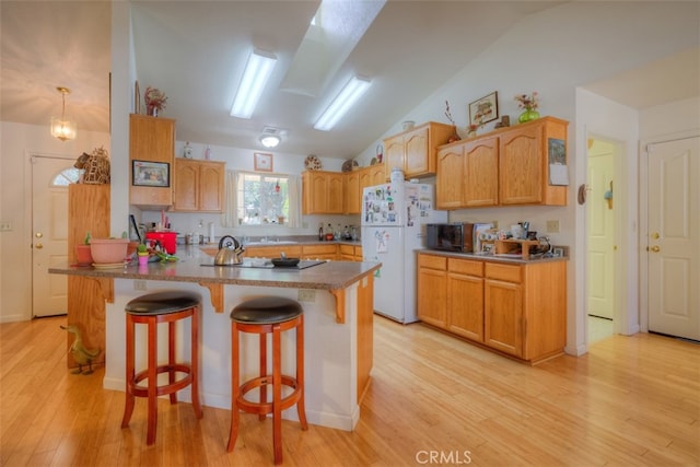 kitchen featuring a breakfast bar area, lofted ceiling with skylight, light wood-type flooring, and white refrigerator