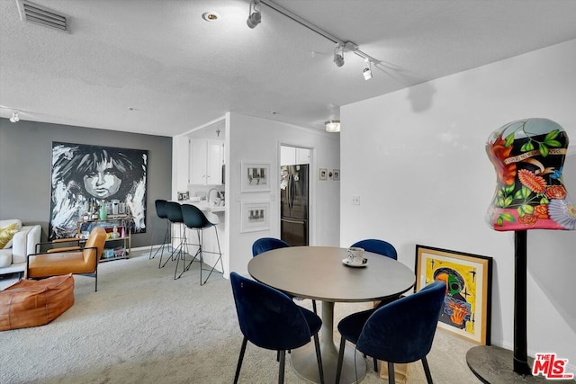 dining area featuring a textured ceiling, light colored carpet, and track lighting