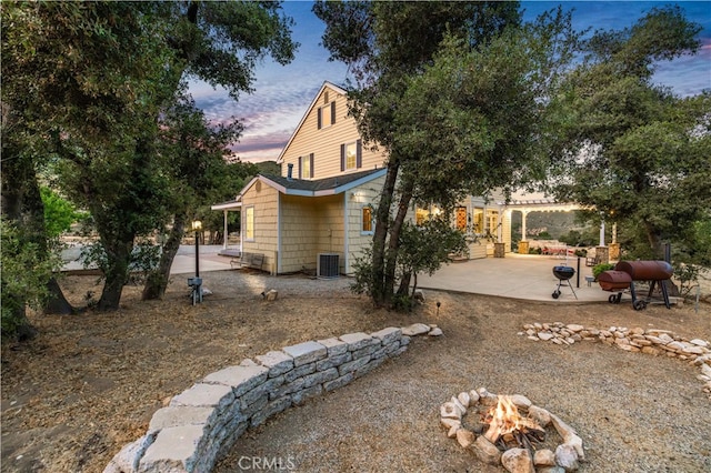 property exterior at dusk with central AC, an outdoor fire pit, a patio area, and a pergola