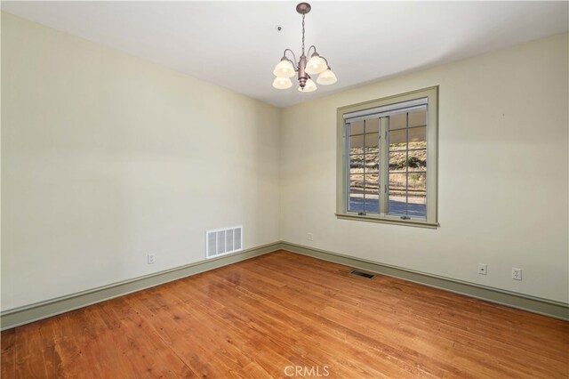 unfurnished room featuring a chandelier and light wood-type flooring